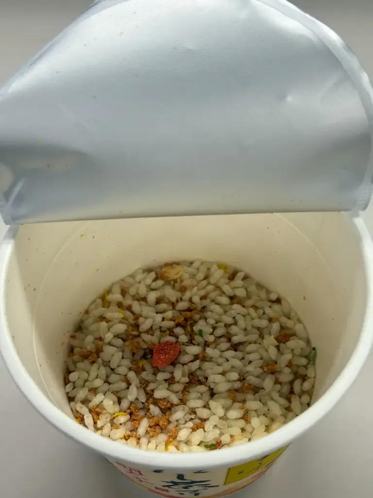 日清だし茶づけ明太子を開封した状態。乾燥ご飯と明太風かまぼこ、卵やねぎが見える。