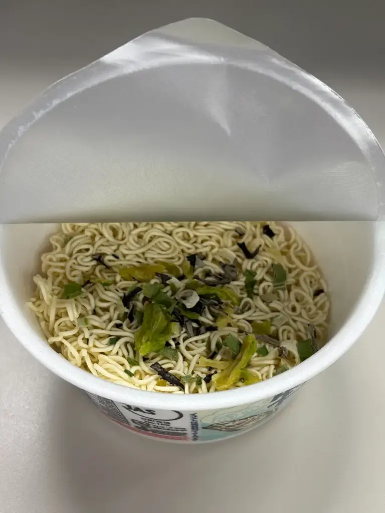 KALDI 限定カップ麺「牡蠣だし塩やきそば」の調理途中写真。かやくを投入し、昆布・キャベツ・ネギなど具材が麺の上に広がっている状態。レビューや口コミ記事の調理工程説明用。