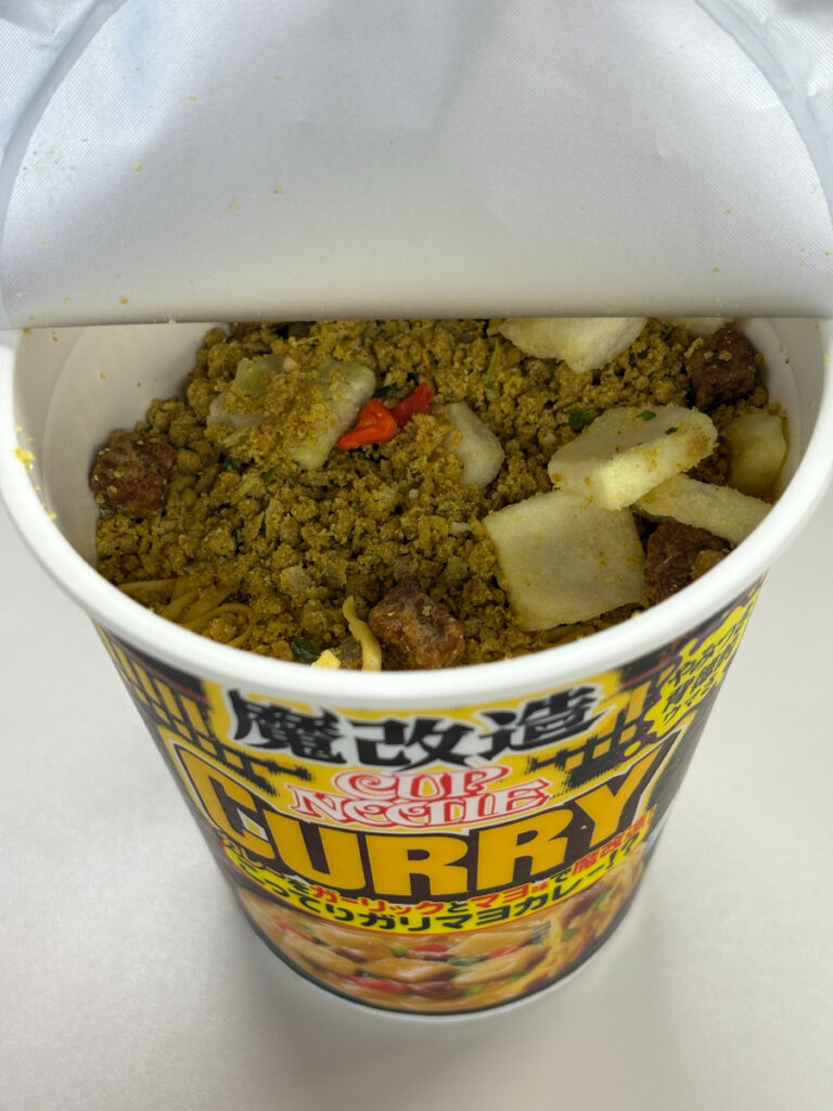 魔改造カップヌードル カレーの開封直後。粉末スープとポテト、謎肉などが眠る“事件現場”の初期状態。