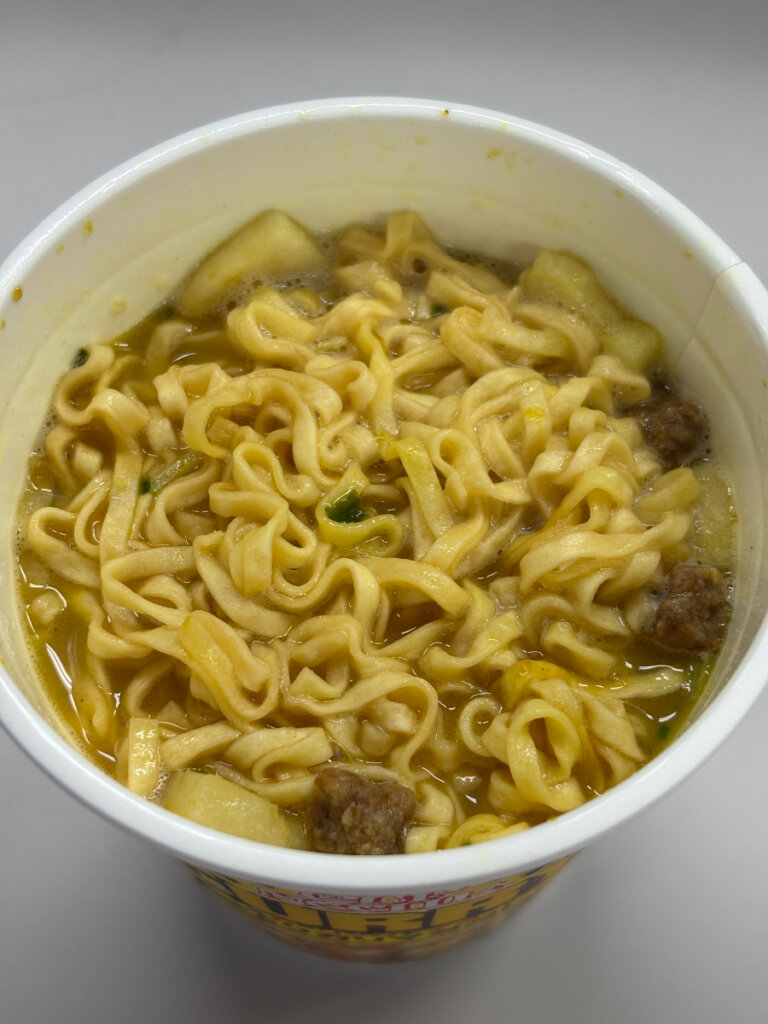 魔改造カップヌードル カレーの完成状態。黄金色のスープに麺が泳ぎ、謎肉やポテトが浮かぶ食欲をそそる仕上がり。