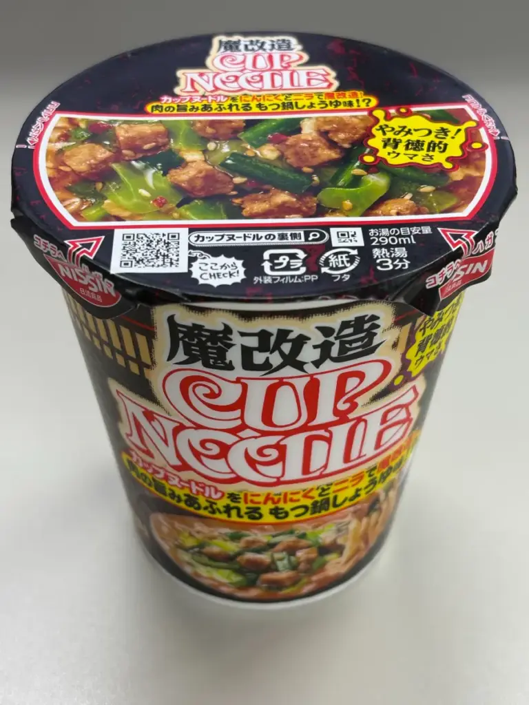 日清 魔改造カップヌードル もつ鍋しょうゆ味の実物パッケージ写真。黒を基調に背徳的なデザインで限定感を強調。