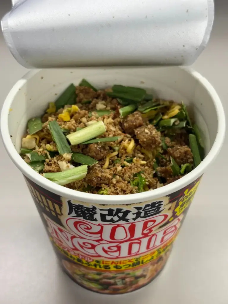 魔改造カップヌードル もつ鍋しょうゆ味を開封した直後の状態。乾燥具材の謎肉やニラが確認できる。